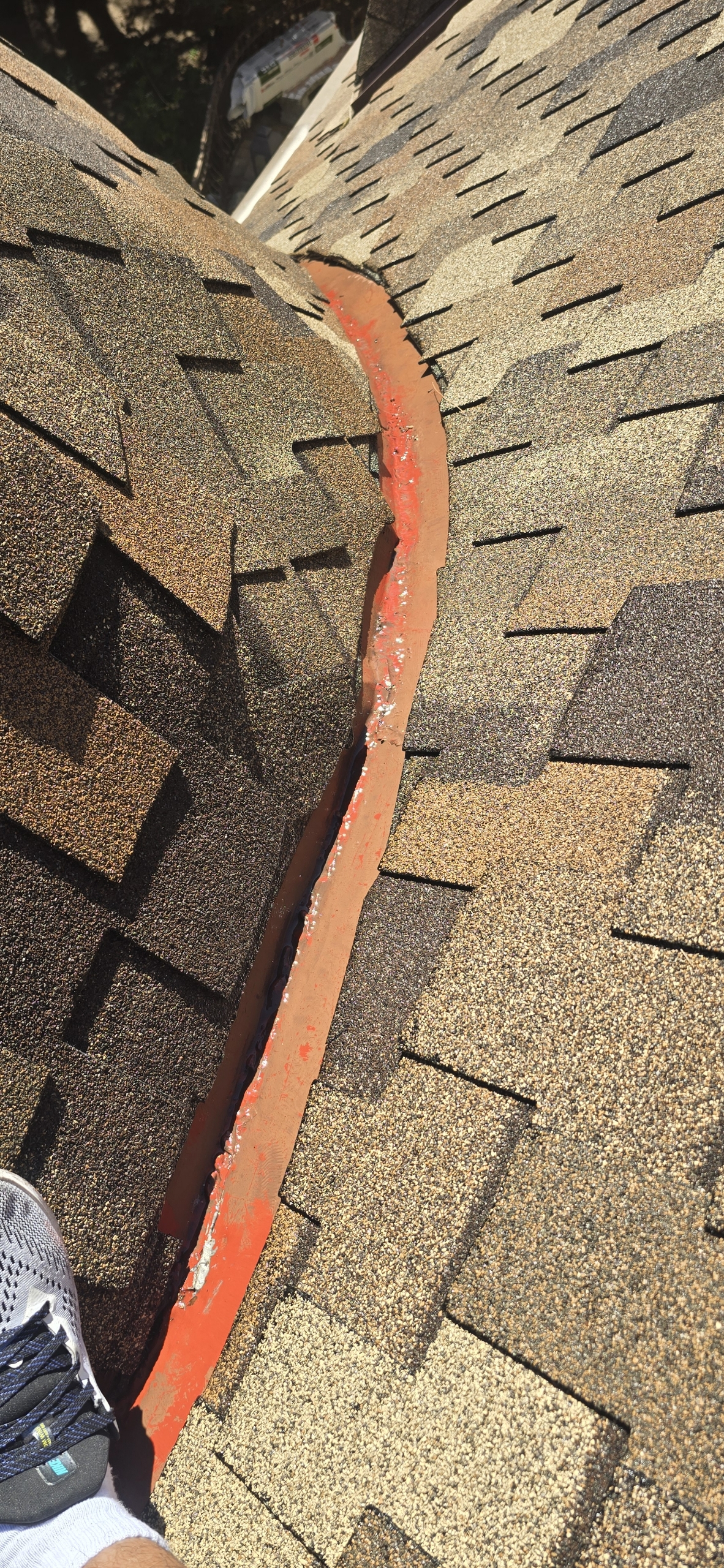 Customer photo: existing painted flashing between shingled roof surfaces, before the proposed repair.